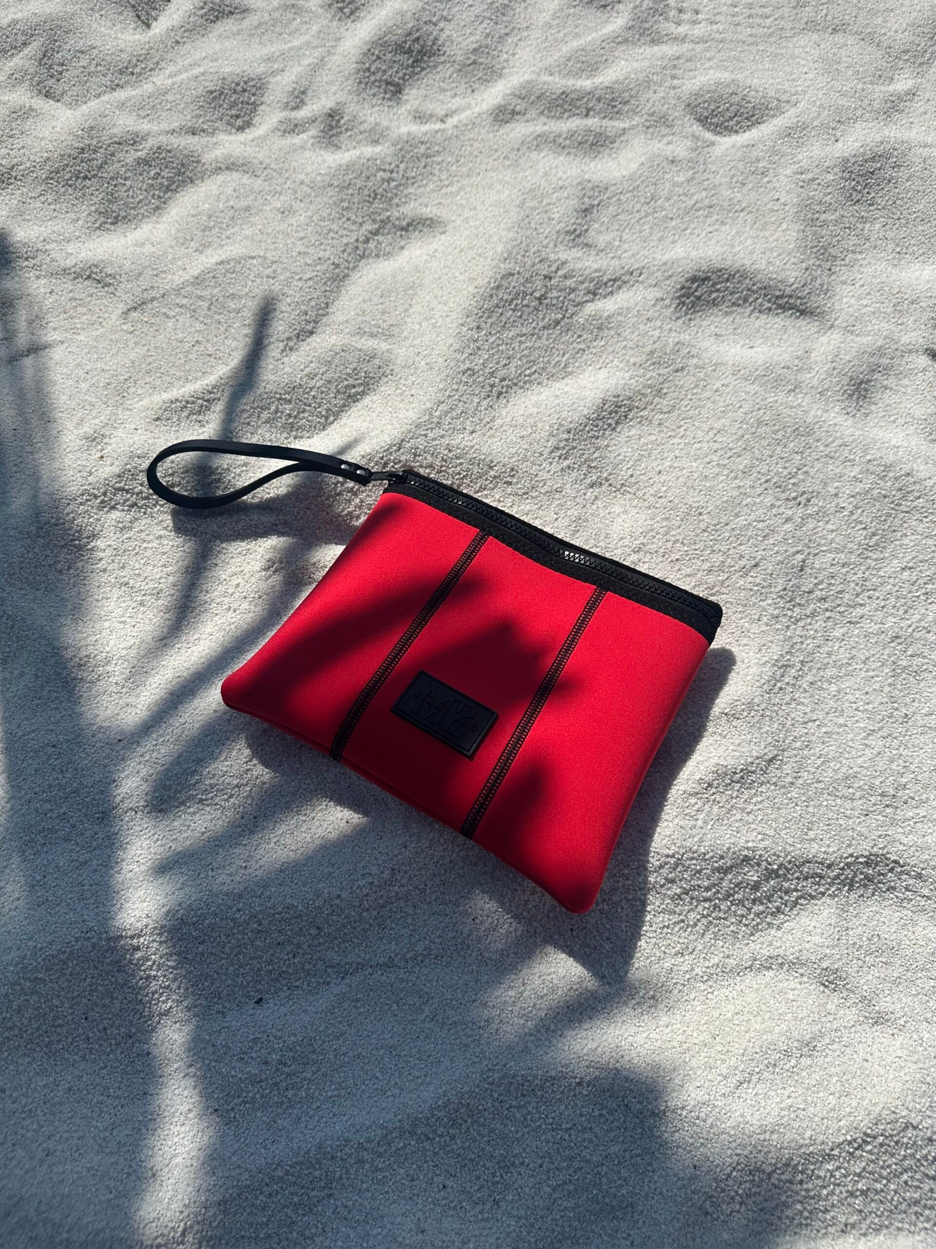 Red pouch with black zipper on sandy surface