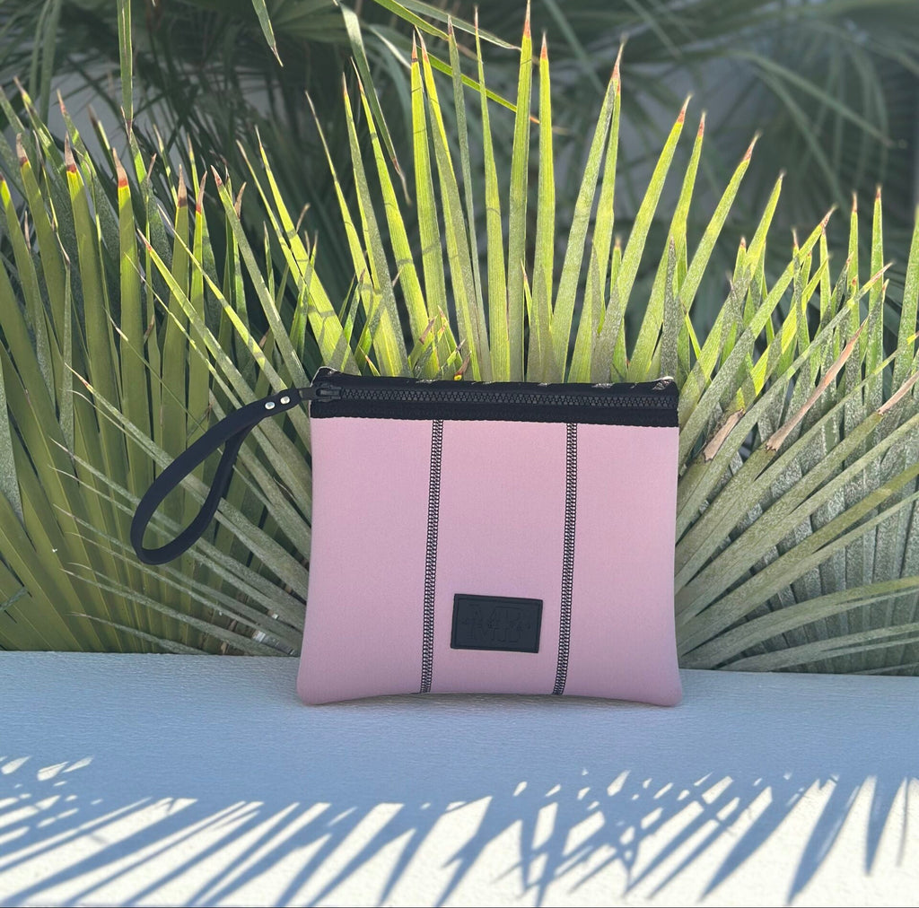 Pink pouch with black zipper and strap on a surface with green plants in the background