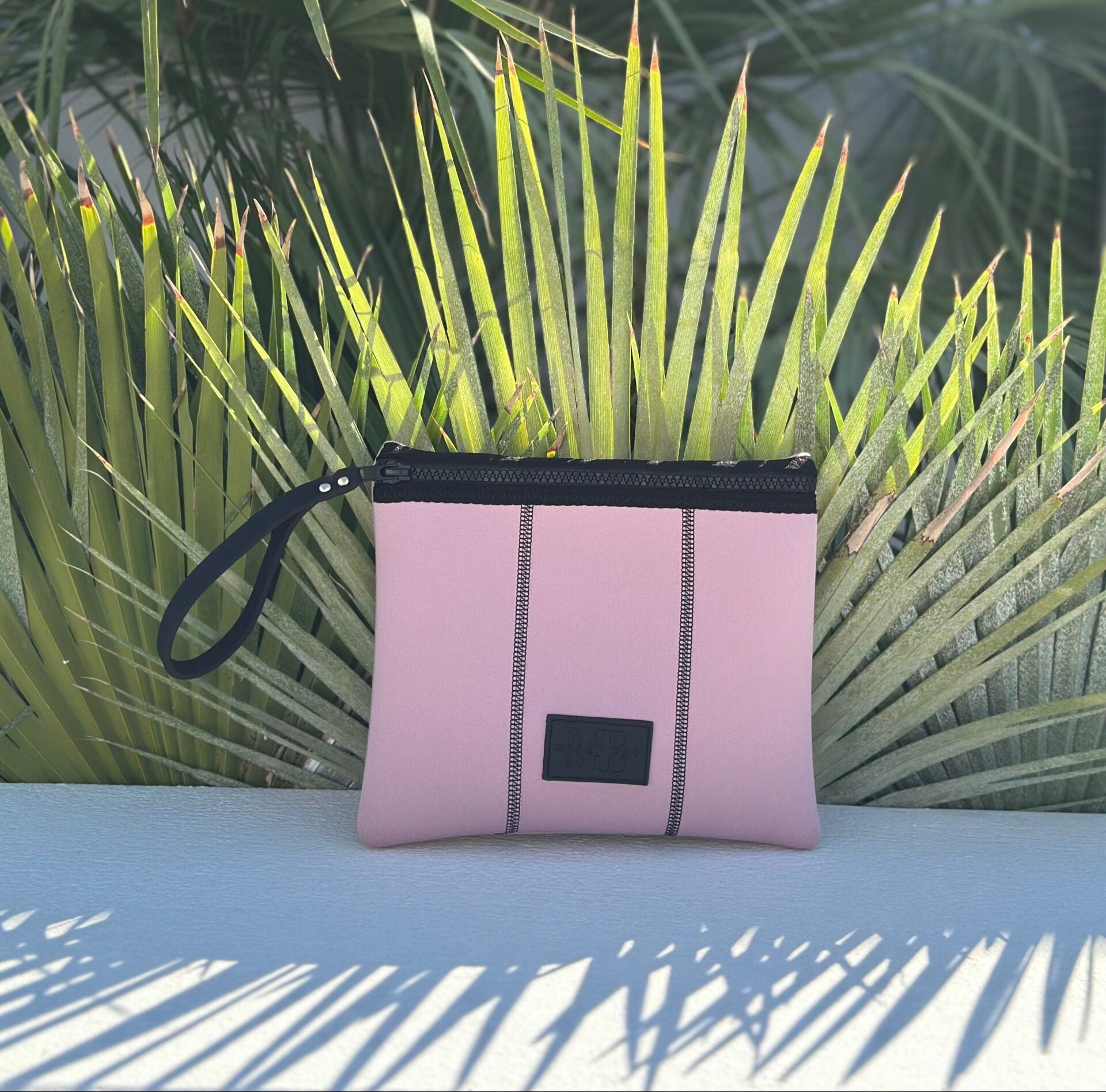 Pink pouch with black zipper and strap on a surface with green plants in the background