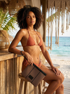 Woman in an orange bikini holding a beige bag on a beach setting