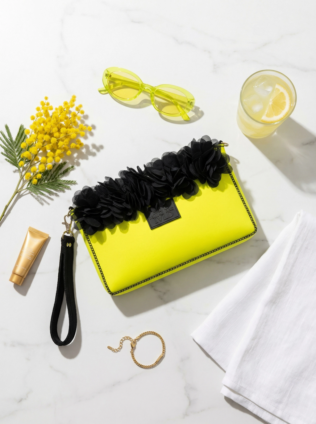 Yellow clutch with black floral accents on a marble surface with accessories.