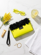 Yellow clutch with black floral accents on a marble surface with accessories.