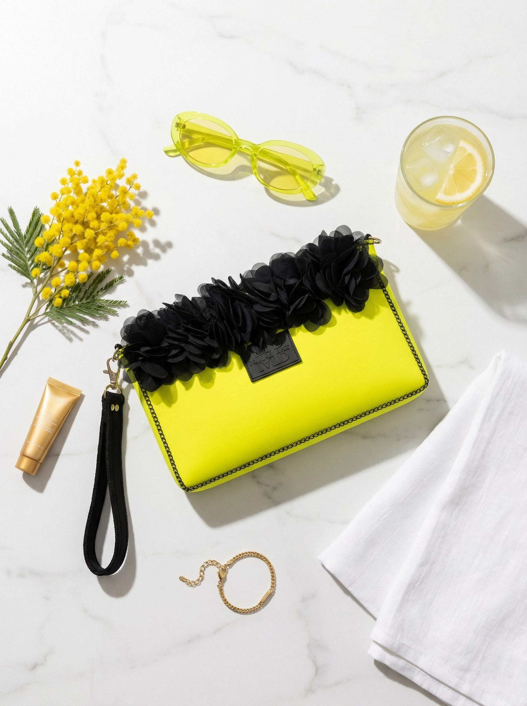 Yellow clutch with black floral accents on a marble surface with accessories.