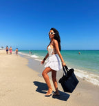 Woman on a beach holding a black bag with people and ocean in the background