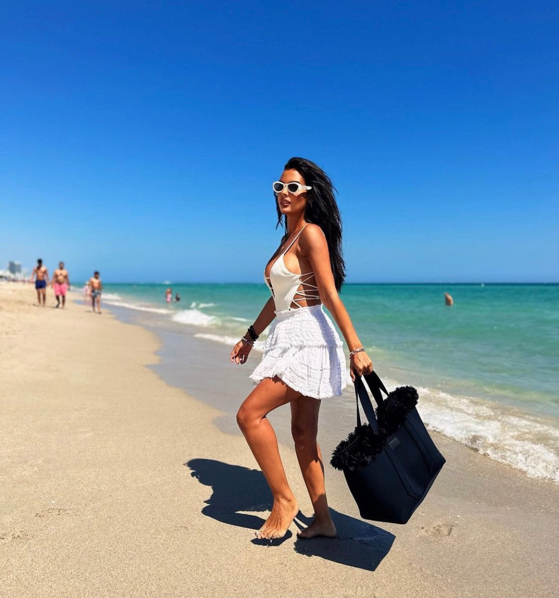 Woman on a beach holding a black bag with people and ocean in the background