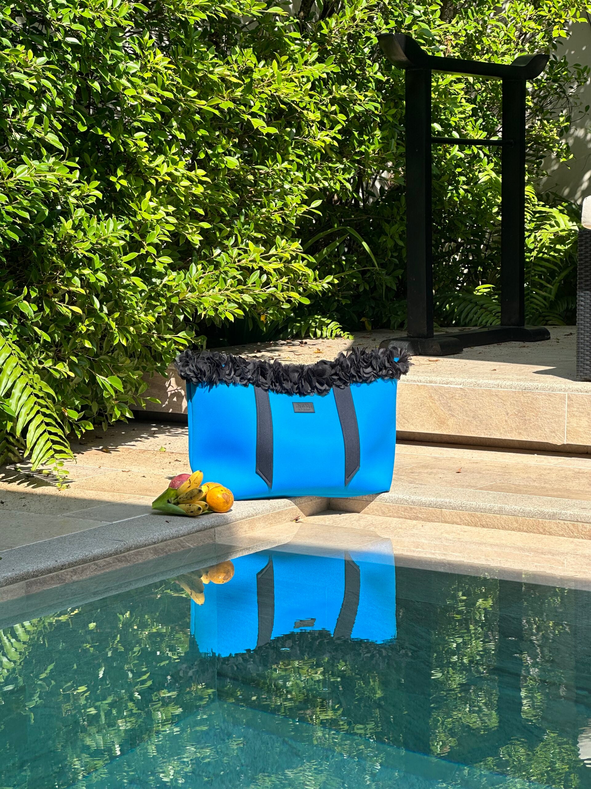 Blue beach tote with black trim on a wooden deck by a pool