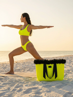 Woman in a yellow bikini on a beach with a yellow and black bag nearby