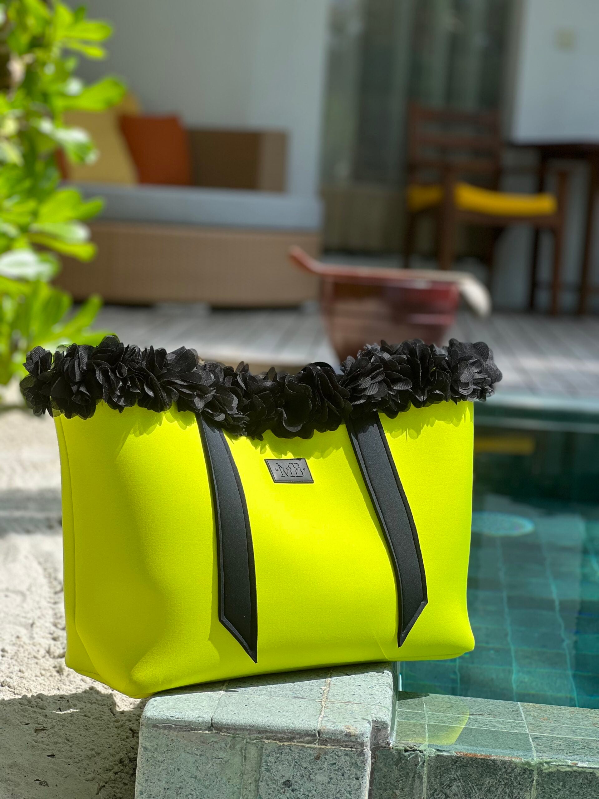 Yellow bag with black floral details on a ledge by a poolside.