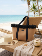 Beige tote bag with black trim on a beach chair by the ocean