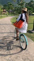 Person riding a bicycle with an orange bag on a path with palm trees in the background