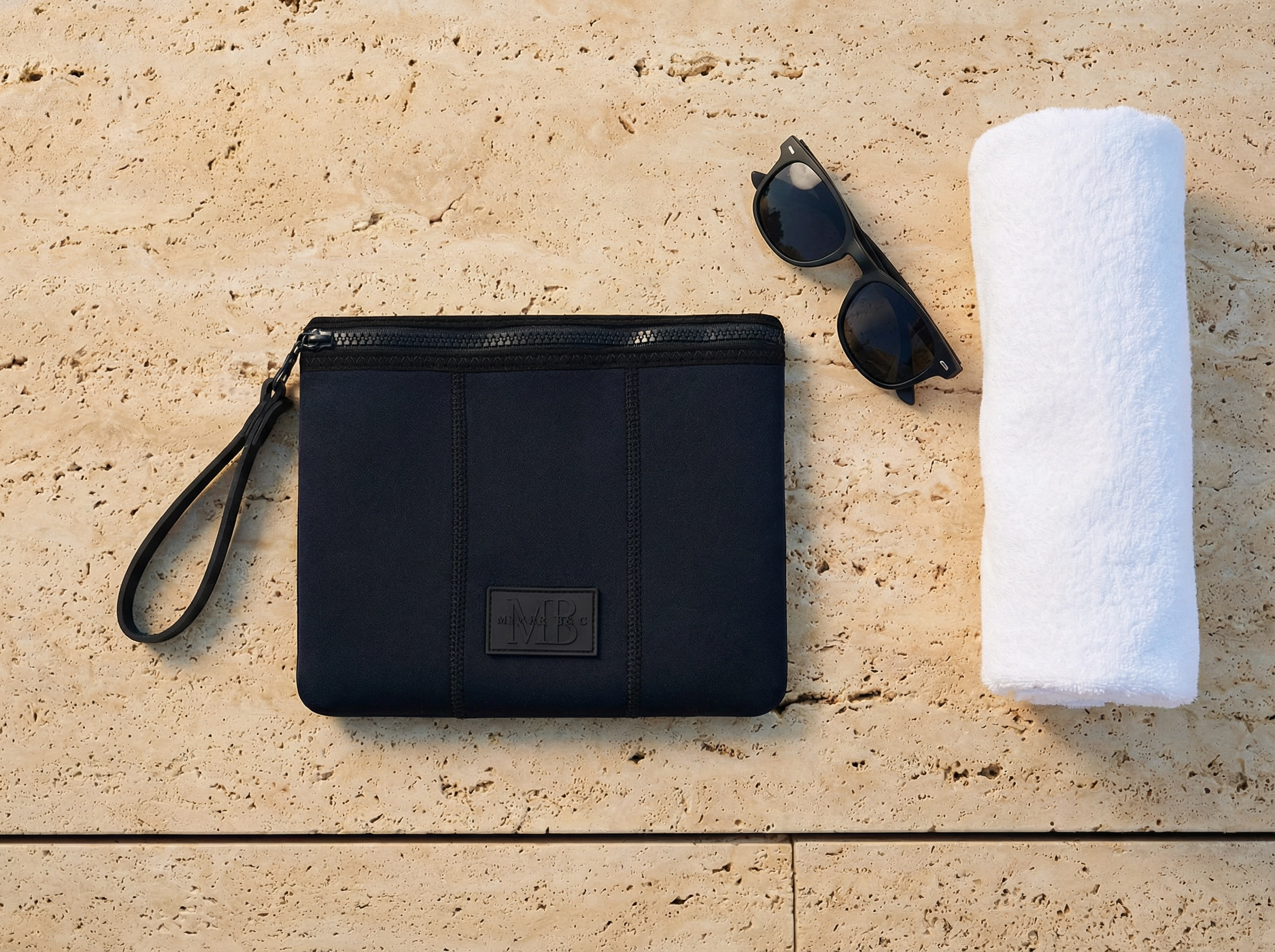 Black pouch, sunglasses, and white towel on a beige stone surface