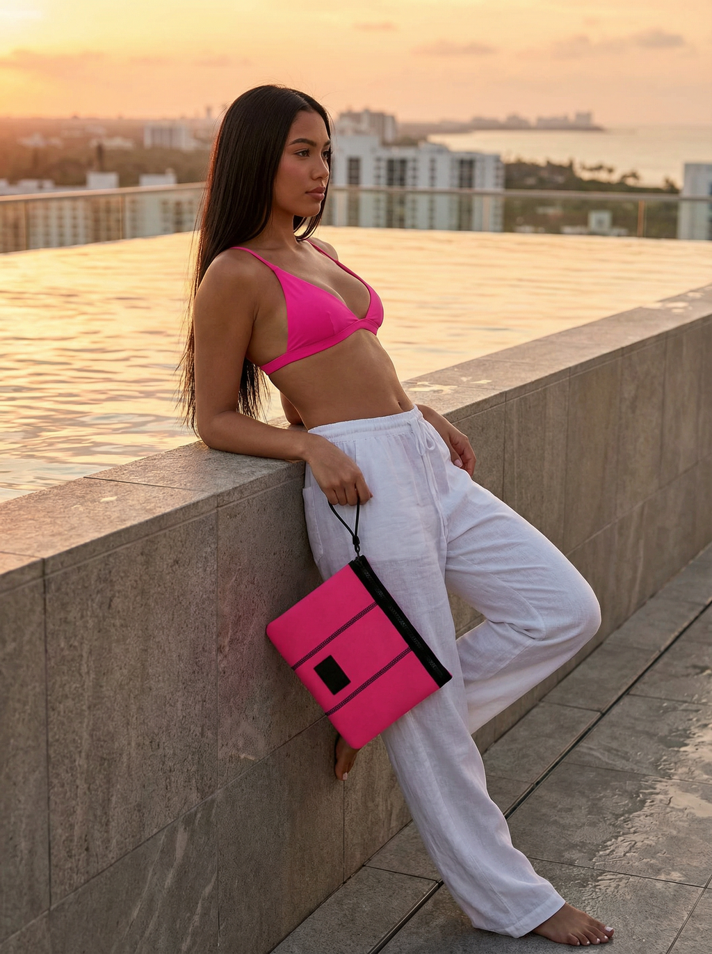Woman in pink top and white pants holding a pink clutch against a cityscape background