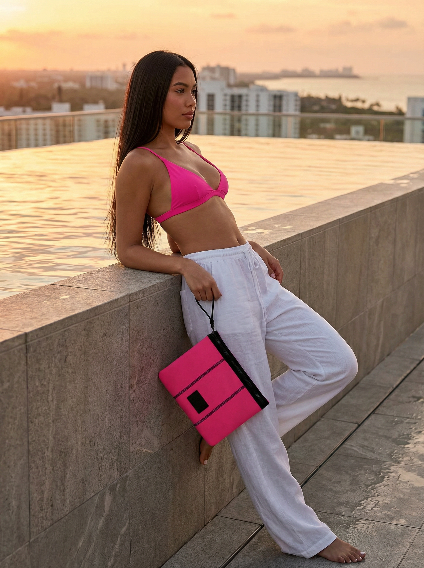 Woman in pink top and white pants holding a pink clutch against a cityscape background