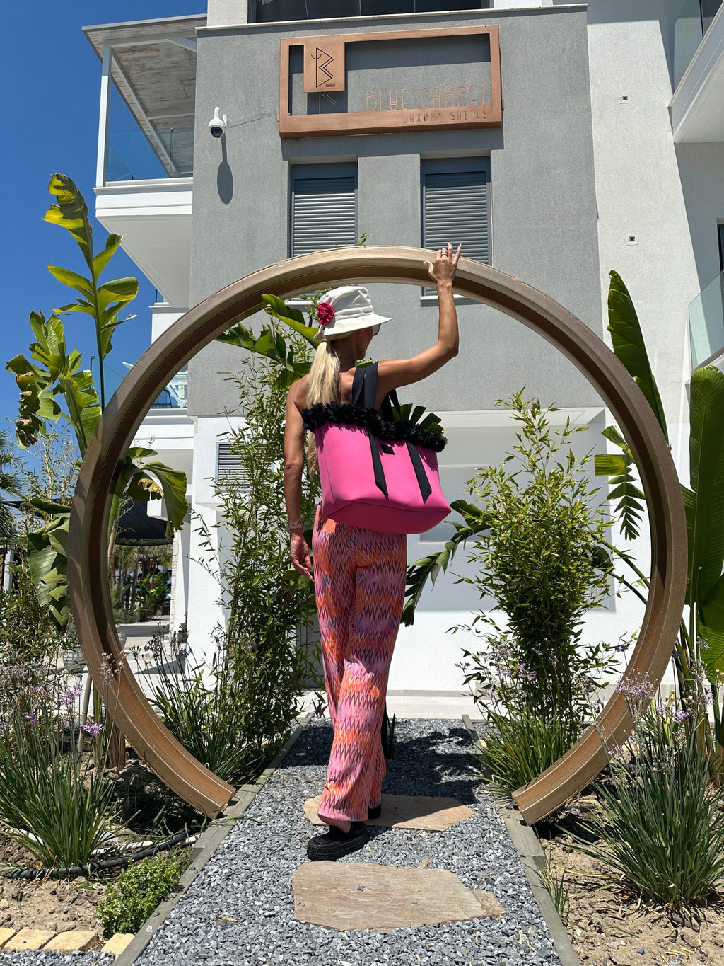 Person standing inside a large circular wooden frame with a building and plants in the background