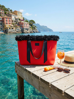 Red tote bag with black trim on a wooden dock by the ocean