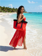 Woman in a red dress holding a large red tote bag on a tropical beach.