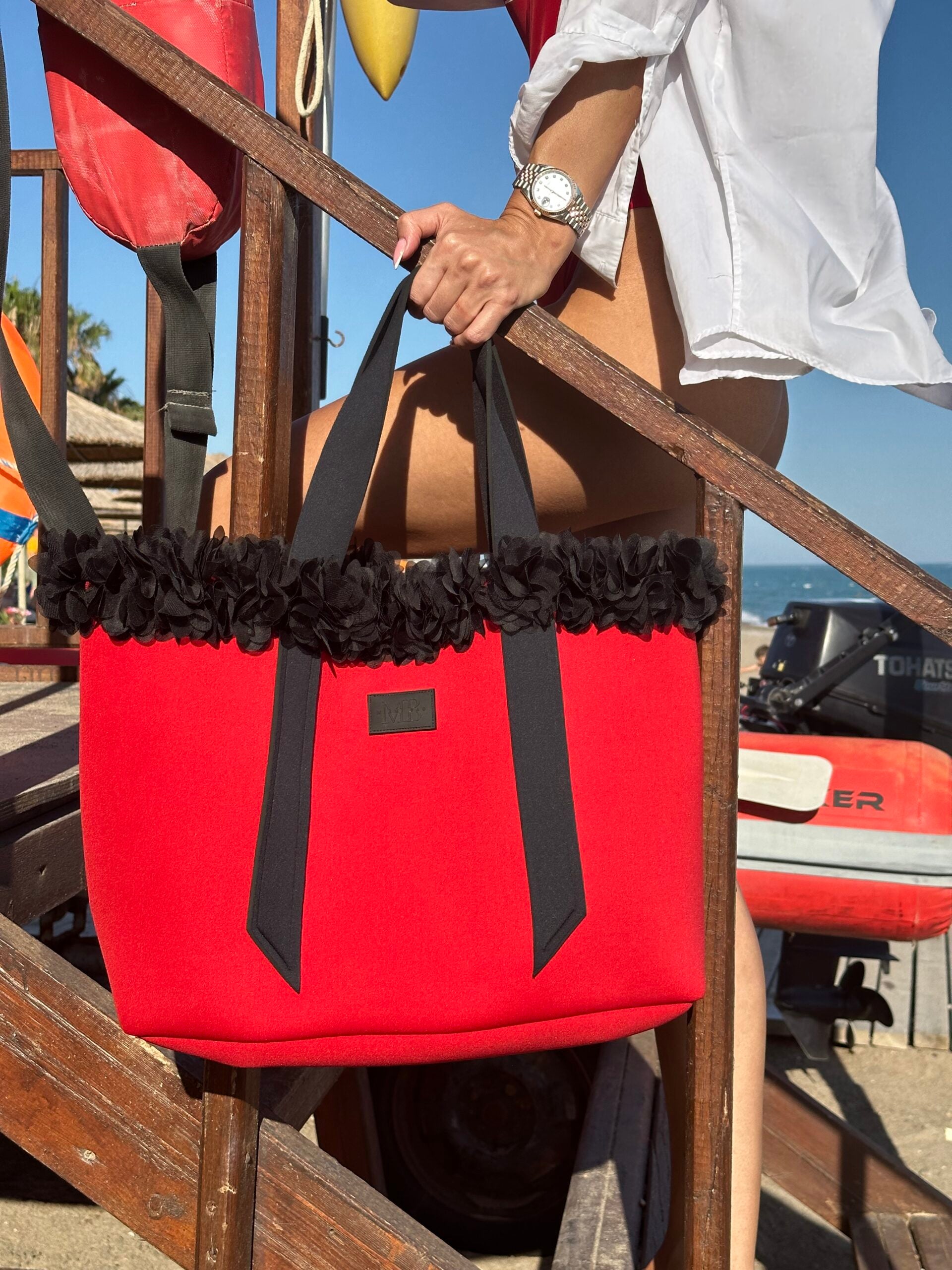 Red tote bag with black trim held by a person on a boat