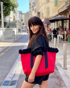 Woman holding a red tote bag with black trim on a city street.